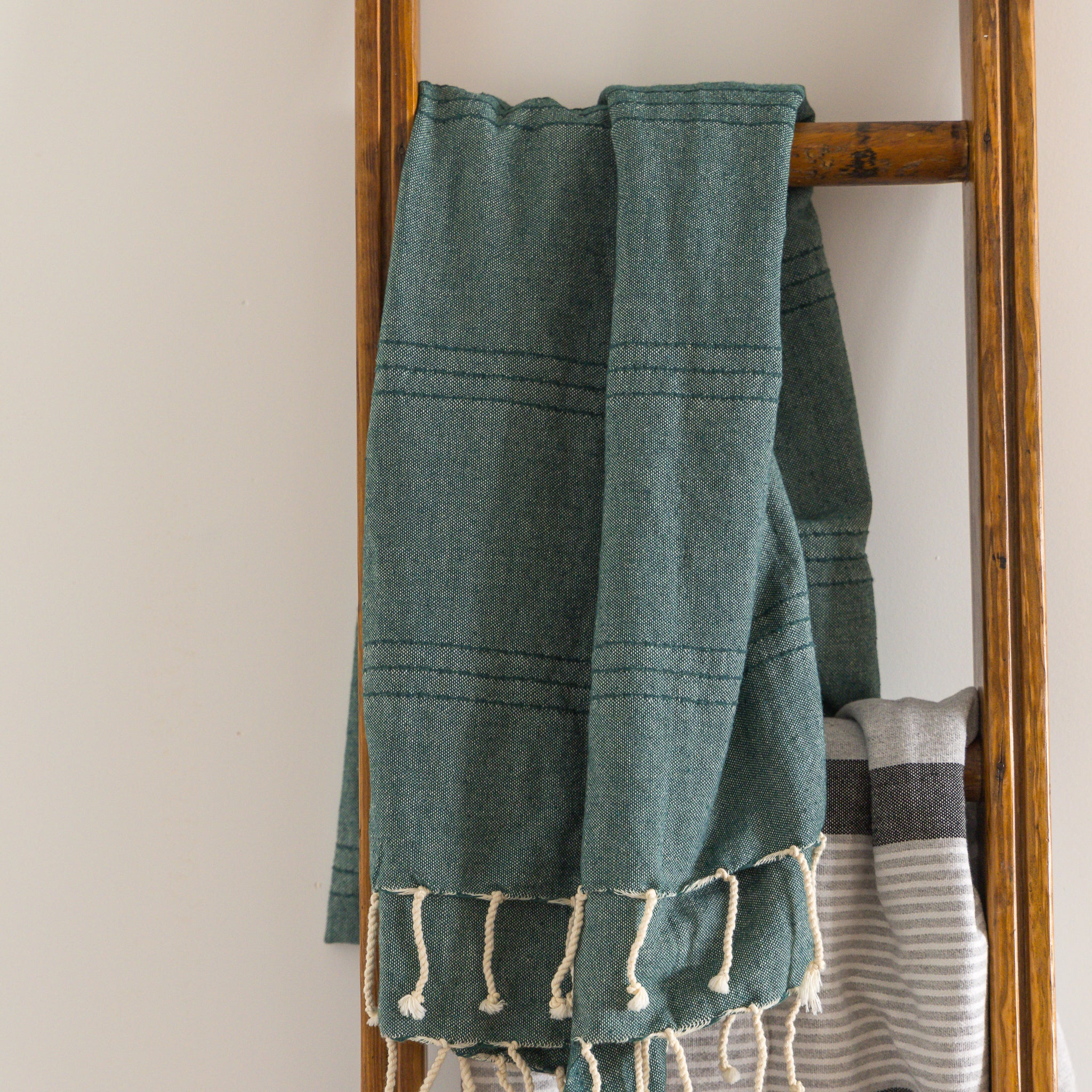A green natural cotton Turkish towel hangs on a ladder