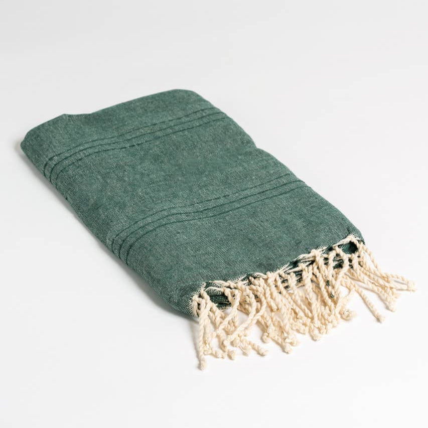 A green natural cotton Turkish towel lays folded