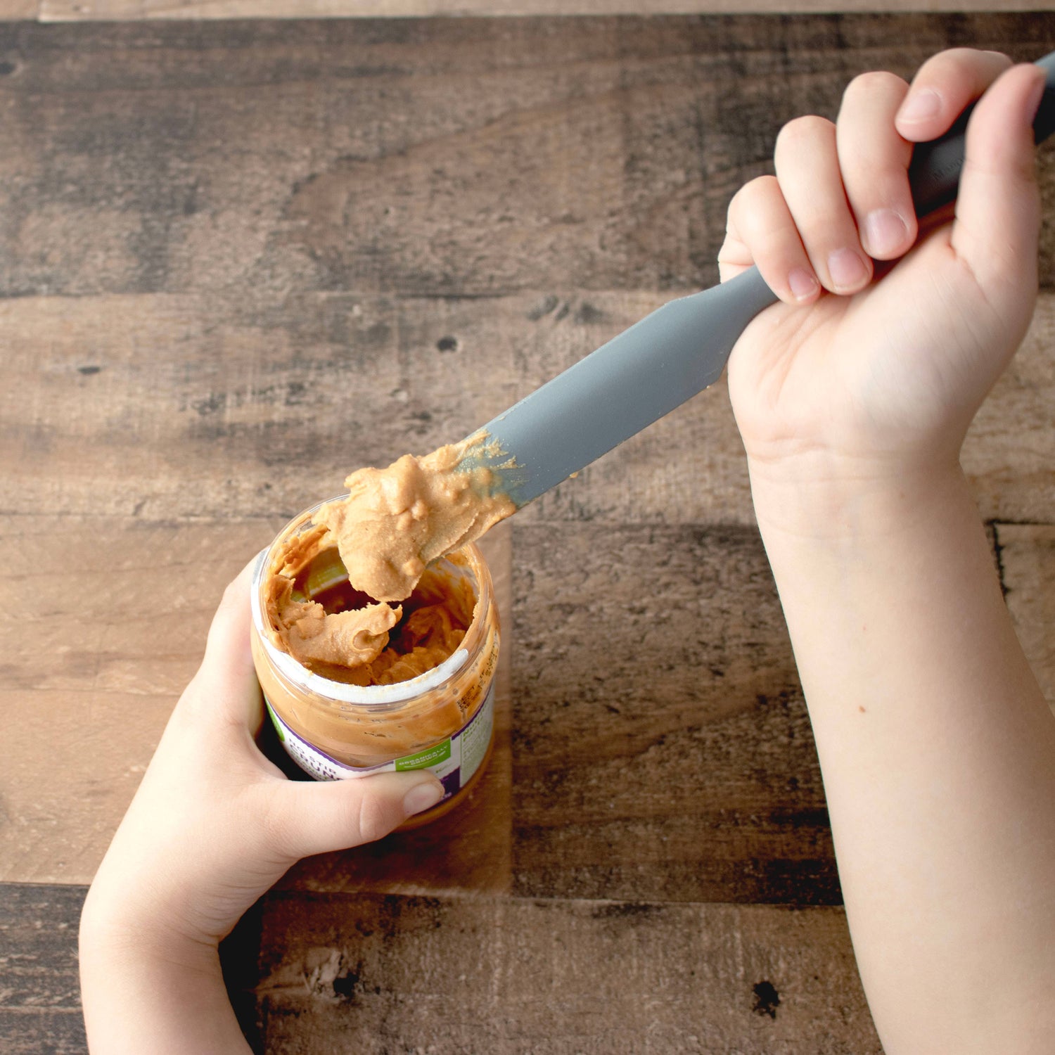 Someone using a sustainable silicone jar scraper for peanut butter