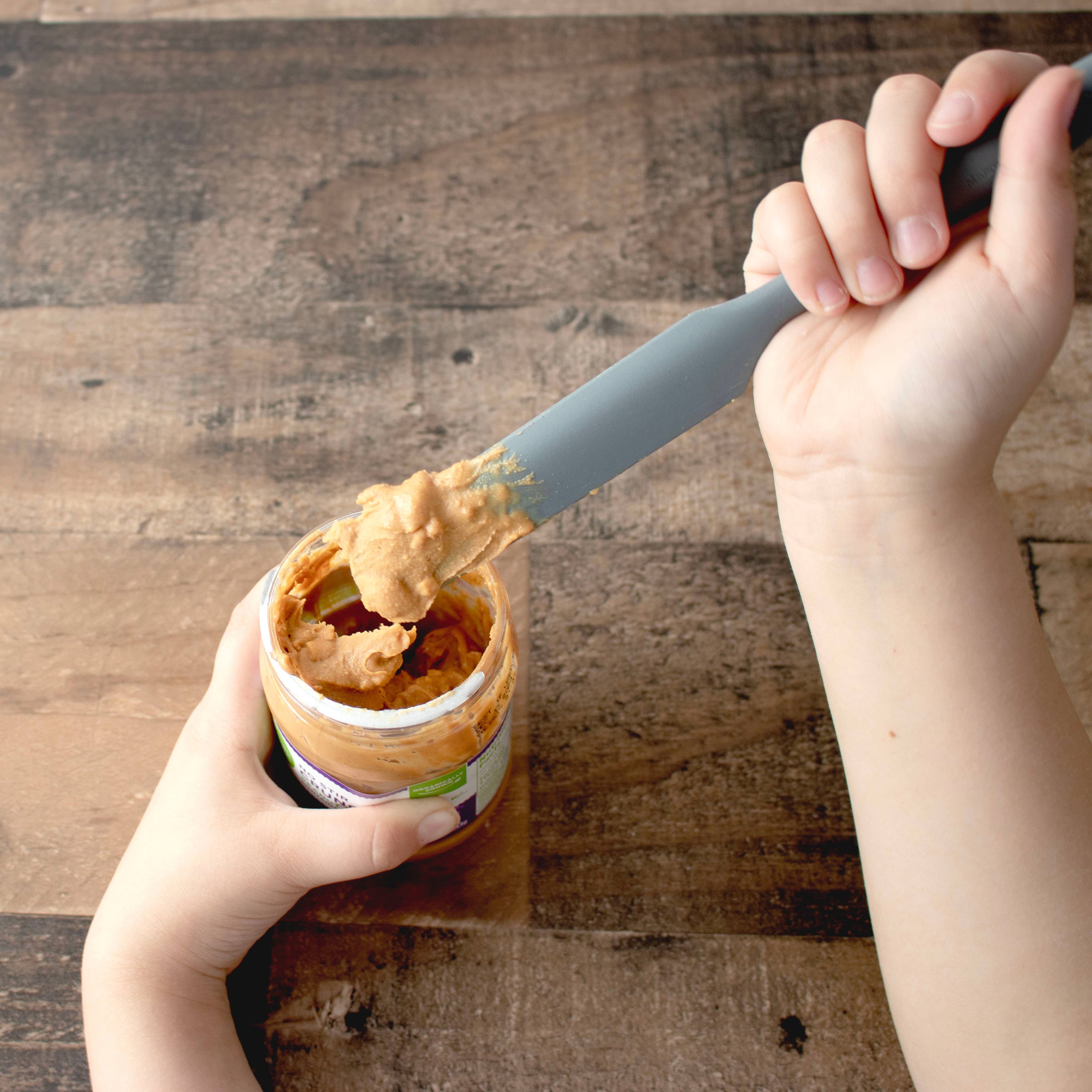 Someone using a sustainable silicone jar scraper for peanut butter