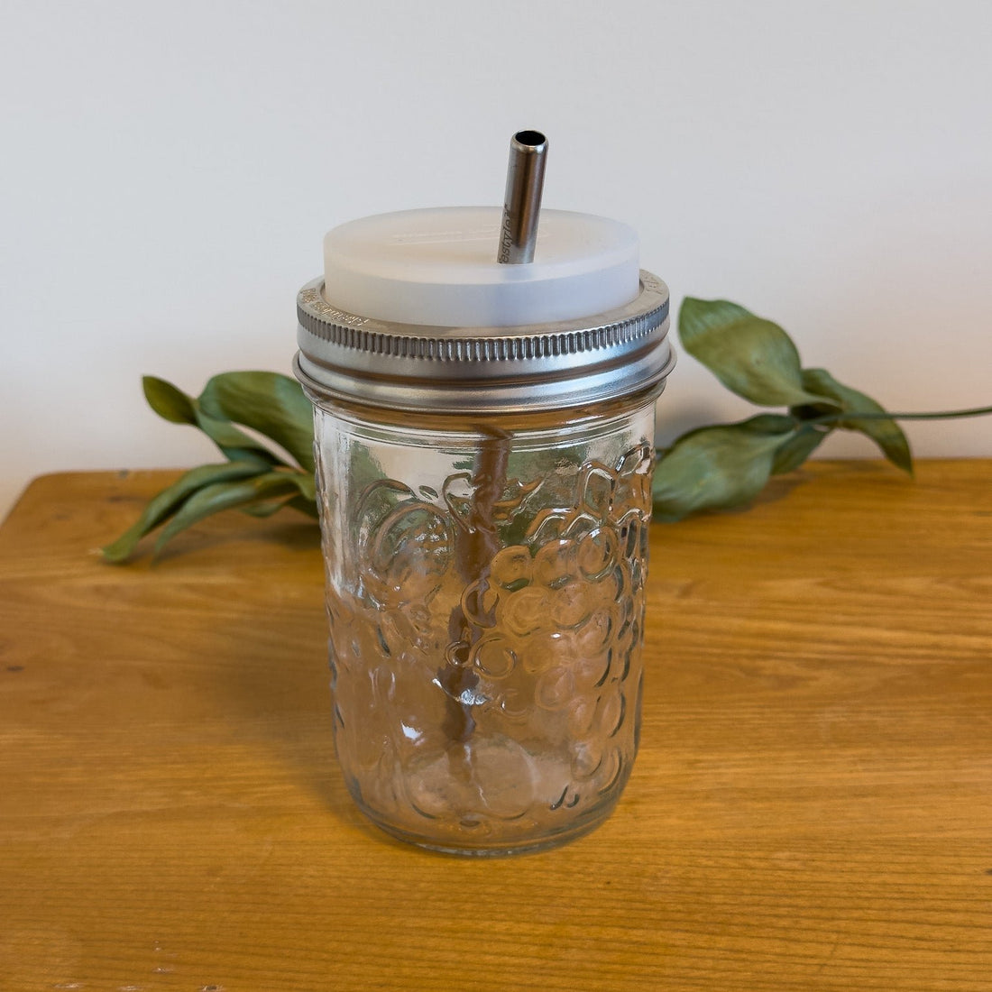 A sustainable silicone tumbler lid on a wide-mouth mason jar with straw