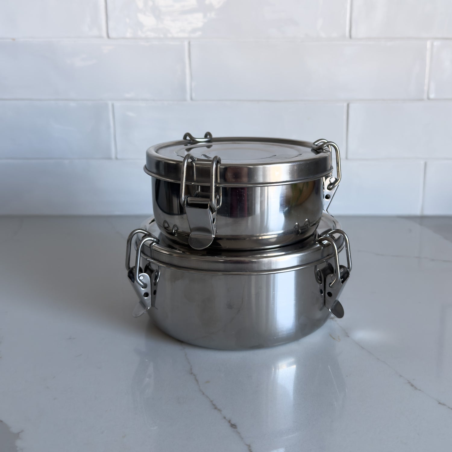 Two sizes of sustainable stainless steel food containers with one stacked on top of the other