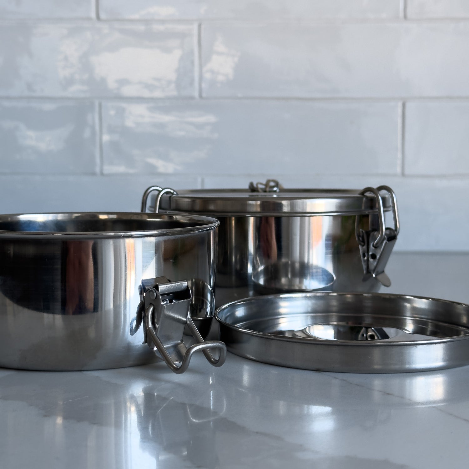 Two sizes of sustainable stainless steel food containers with one open and the lid off to one side