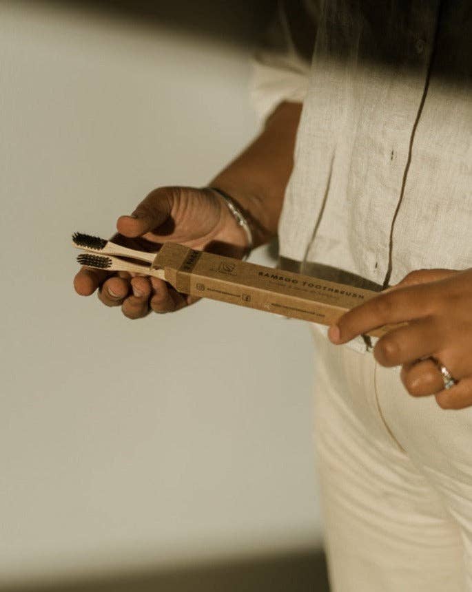 A person opening a box of two bamboo toothbrushes