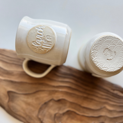 Two handmade mugs by Melba Seto featuring the Larch Life logo, one is turned on its side and the other upside-down to show the bottom