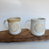 Two handmade mugs by Melba Seto featuring the Larch Life logo