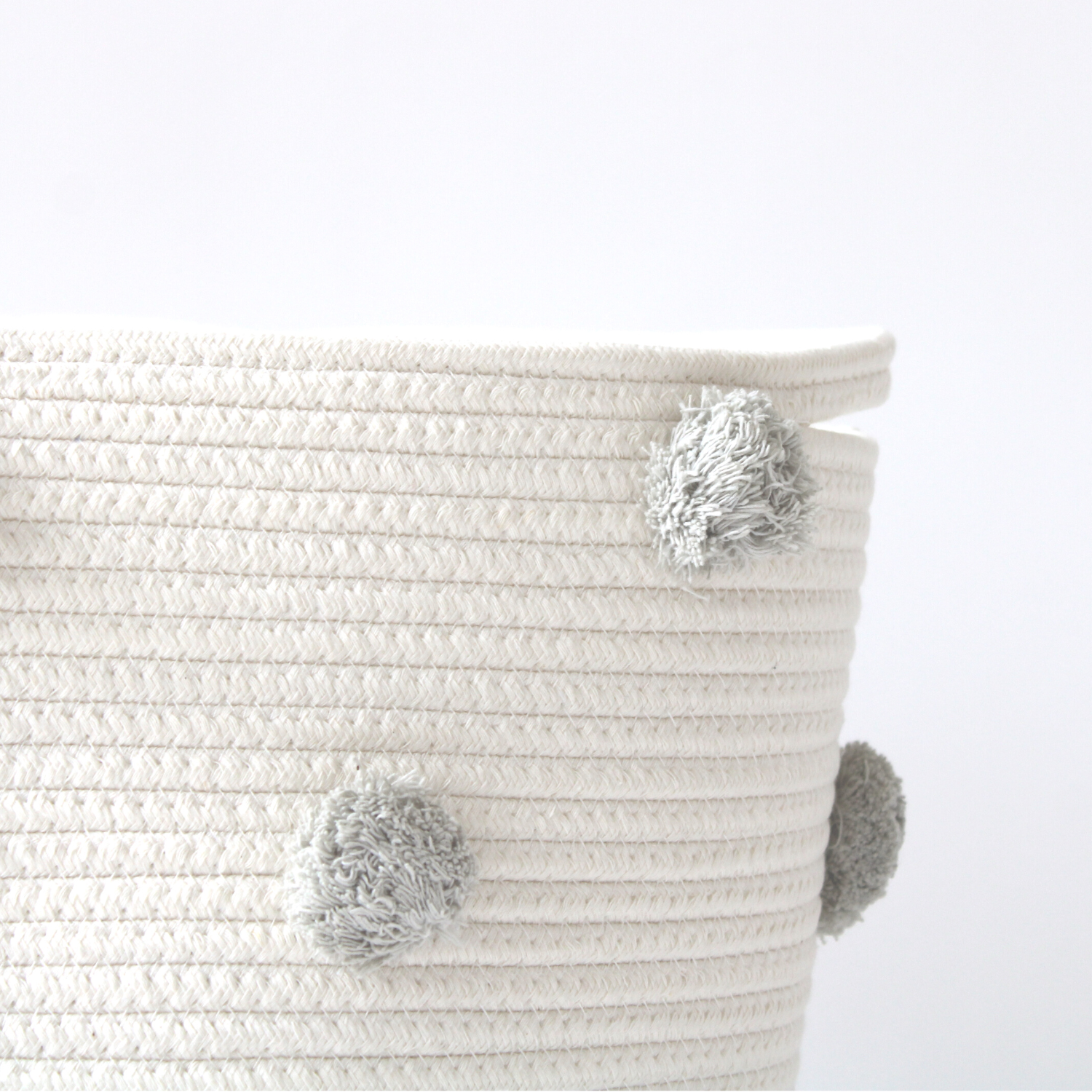 A close-up of a large handmade cotton basket with grey pom-poms shows texture