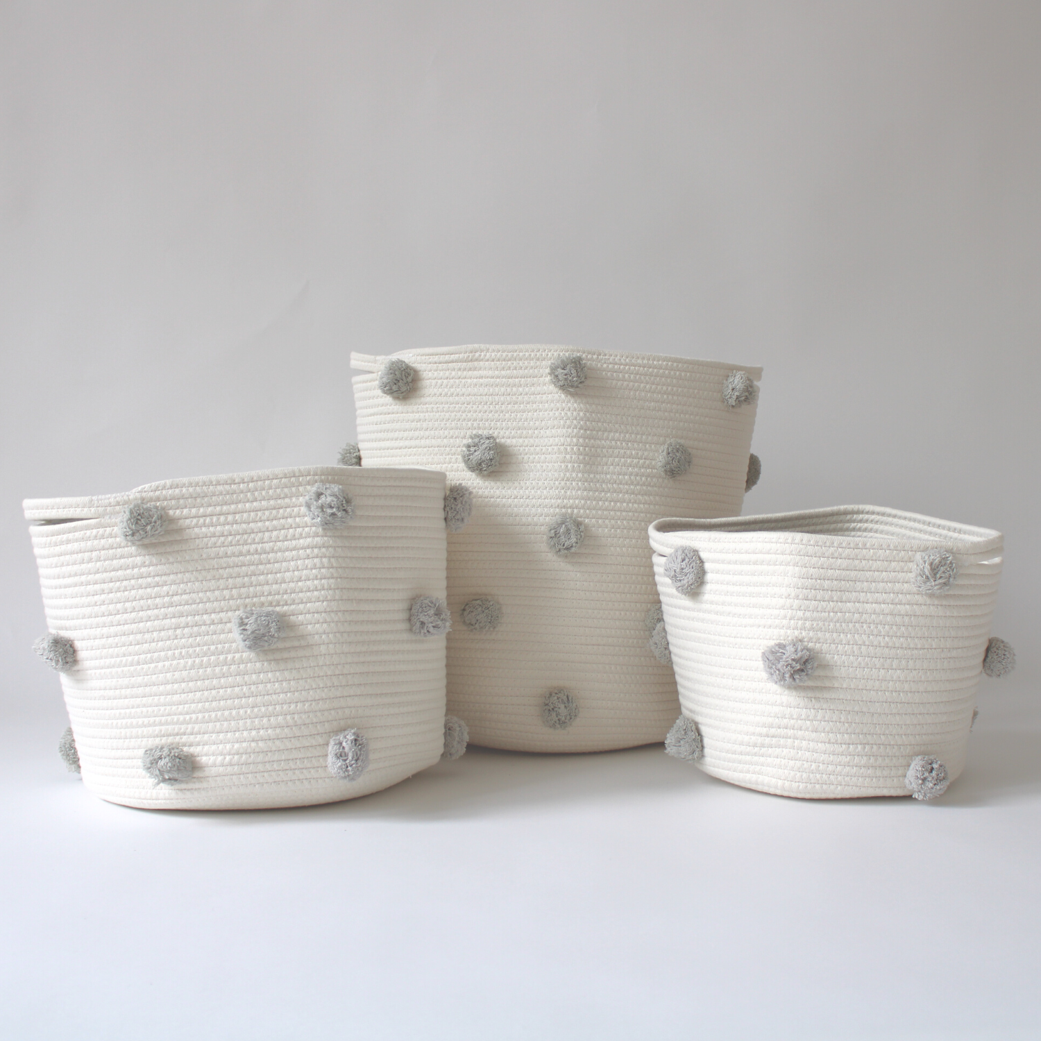 A trio of handmade cotton baskets with grey pom-poms in various sizes