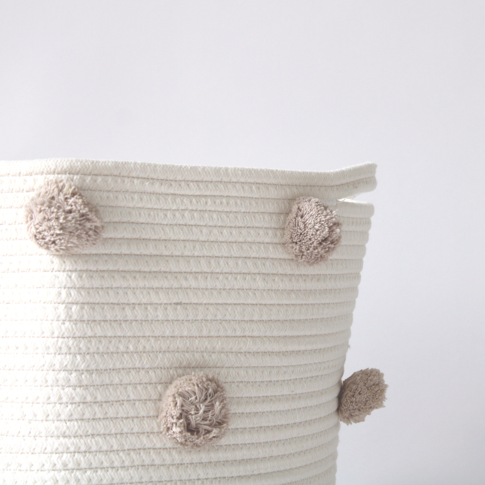 A close-up of a handmade cotton basket with taupe pom-poms showing texture