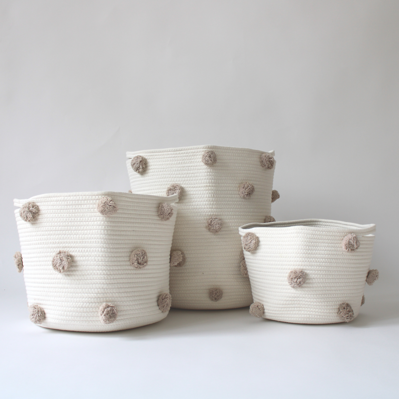 A trio of handmade cotton rope baskets with taupe pom-poms in various sizes