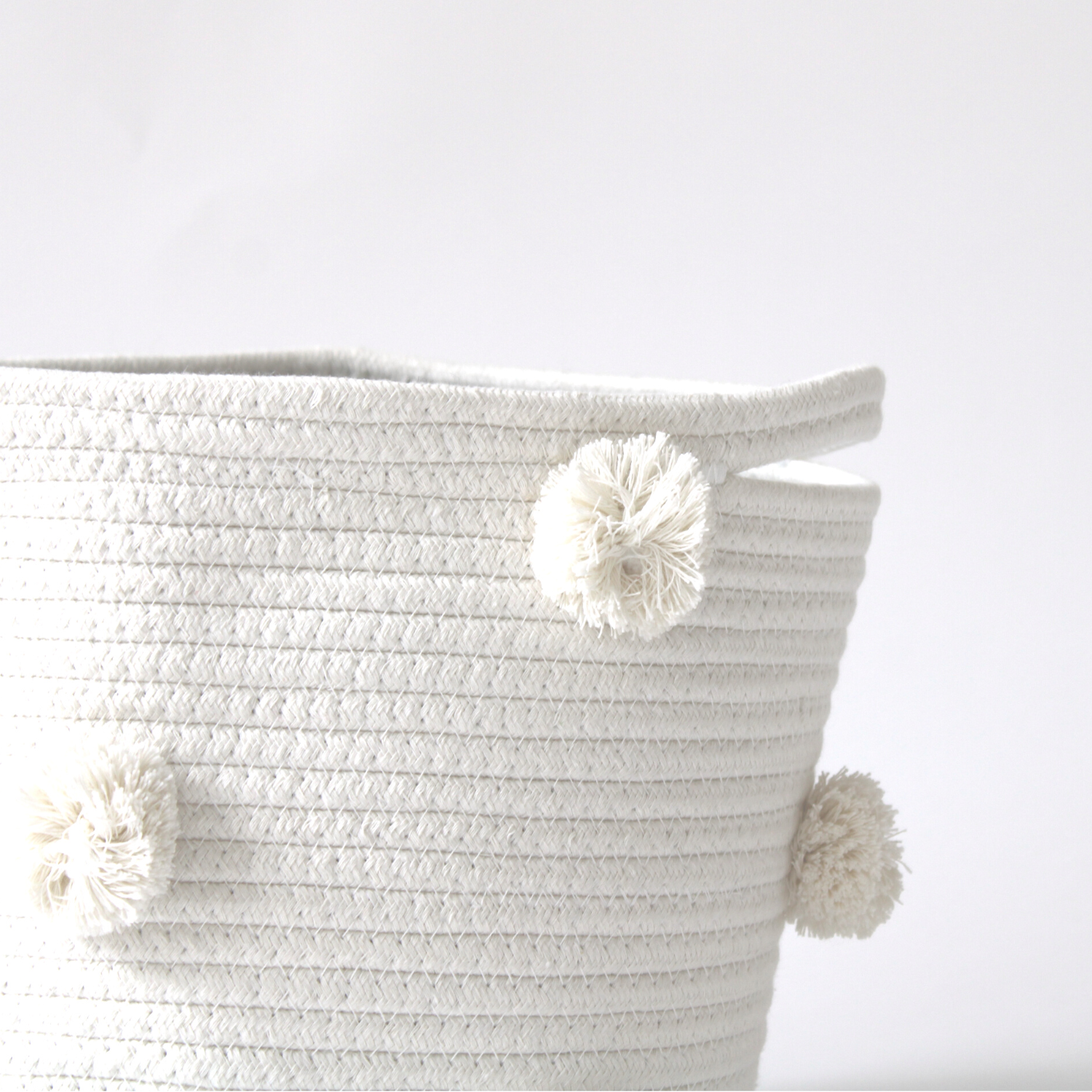 A close-up of a handmade natural cotton basket with white pom-poms showing texture