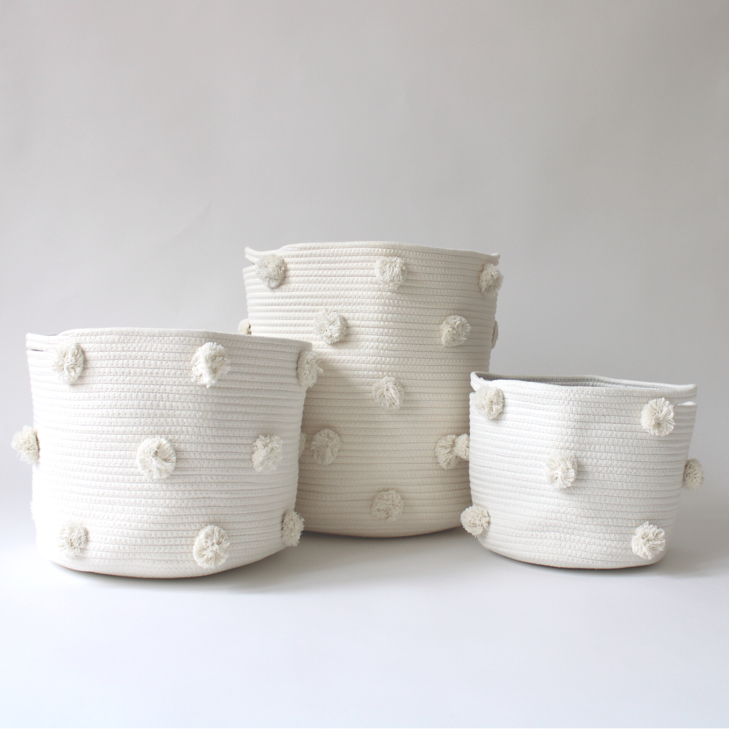 A trio of handmade natural cotton baskets with white pom-poms