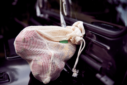 A natural cotton mesh bag filled with produce sitting on the hood of a vehicle