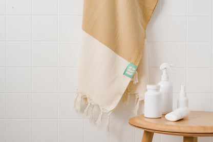 A mustard yellow Turkish bath towel hangs near bath products