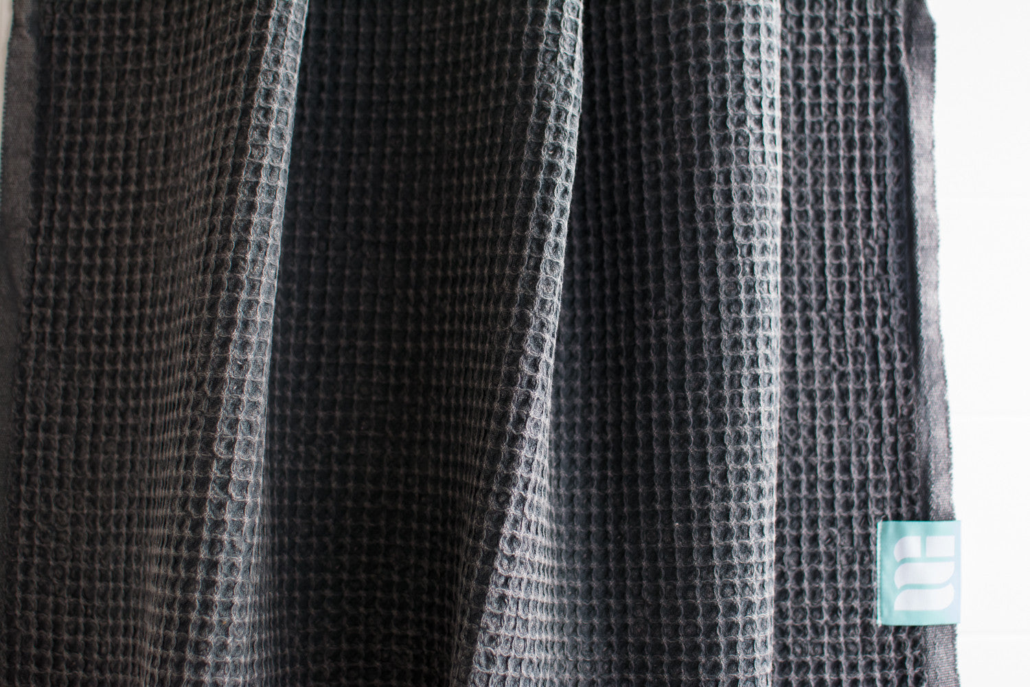 A close up showing the waffle texture of a natural cotton Turkish bath towel in dark grey