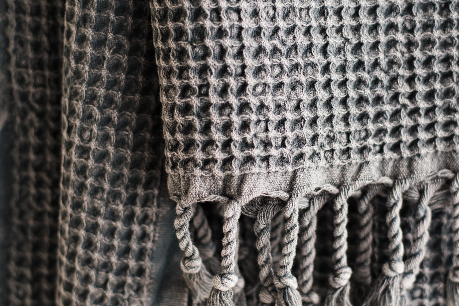 A close up showing the waffle texture of a natural cotton Turkish hand towel in dark grey