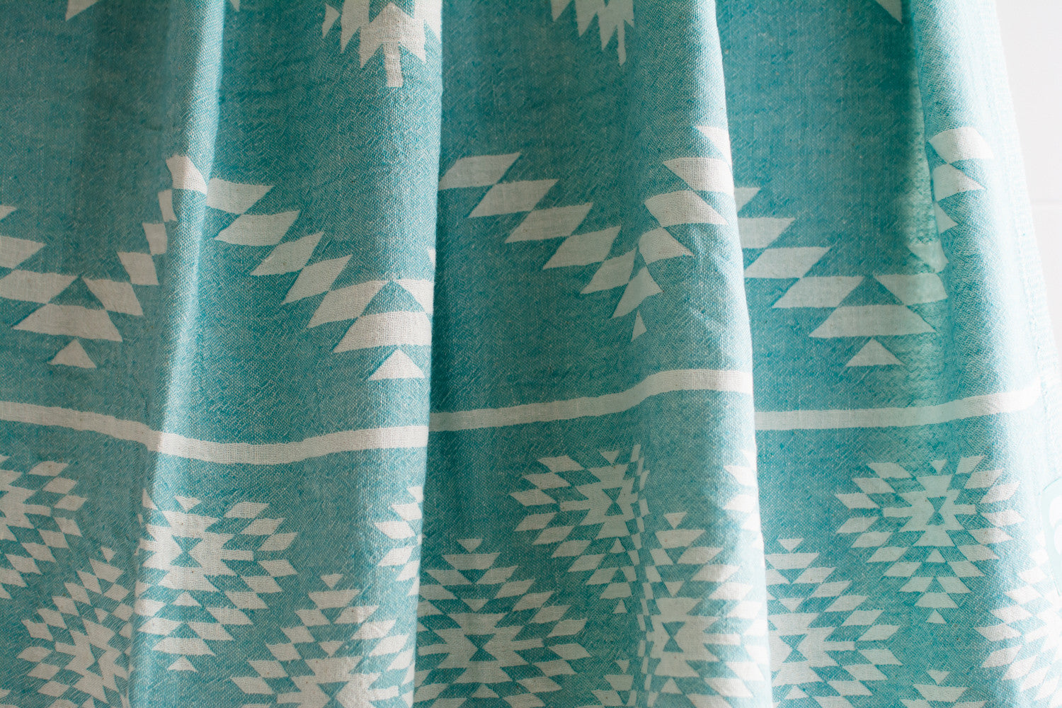 A close up of a medium weight Turkish bath towel in teal with geometric pattern showing texture