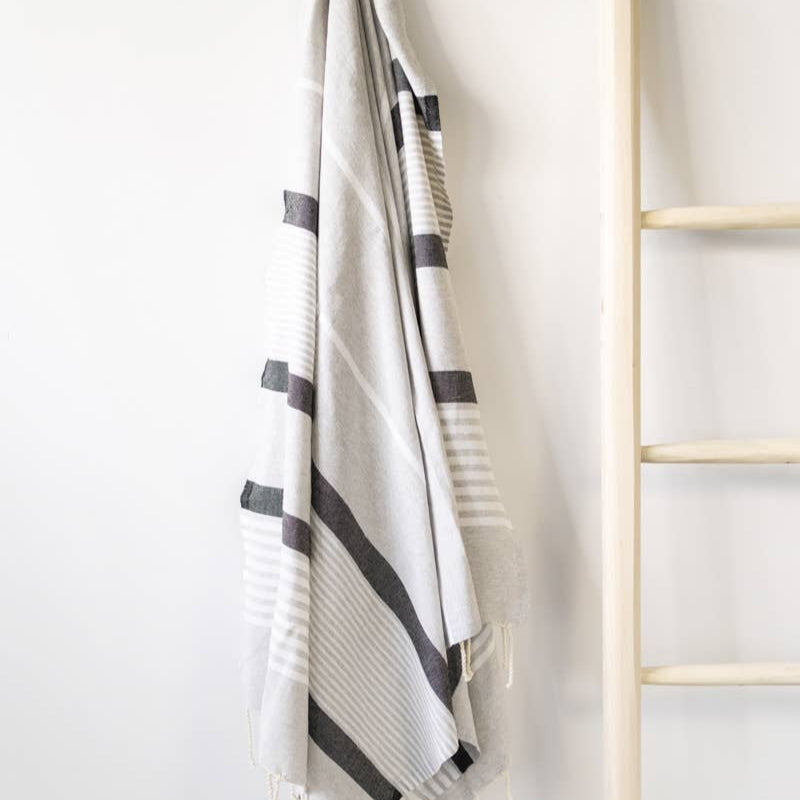 A grey and white striped natural cotton Turkish towel hangs on a ladder