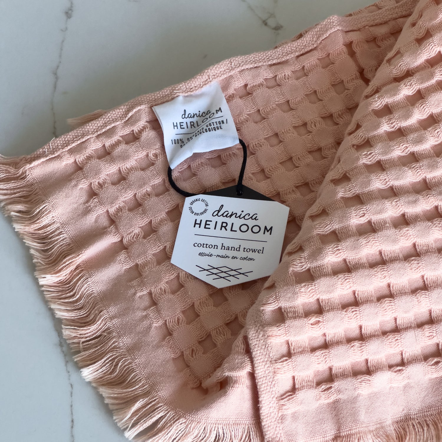 A detail shot of a blush pink waffle-weave organic cotton hand towel