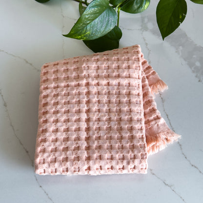 A blush pink waffle-weave organic cotton hand towel