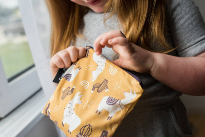 A young child holding a llama-themed large reusable zip bag