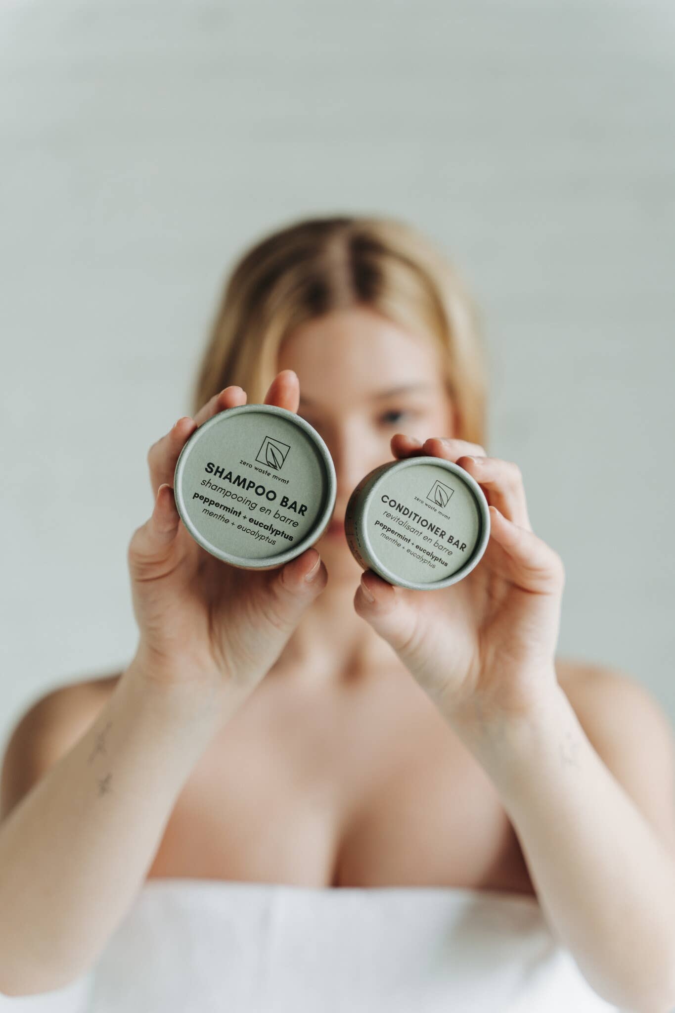 A person holds the packaging for both a sustainable solid shampoo and conditioner bar in front of their face