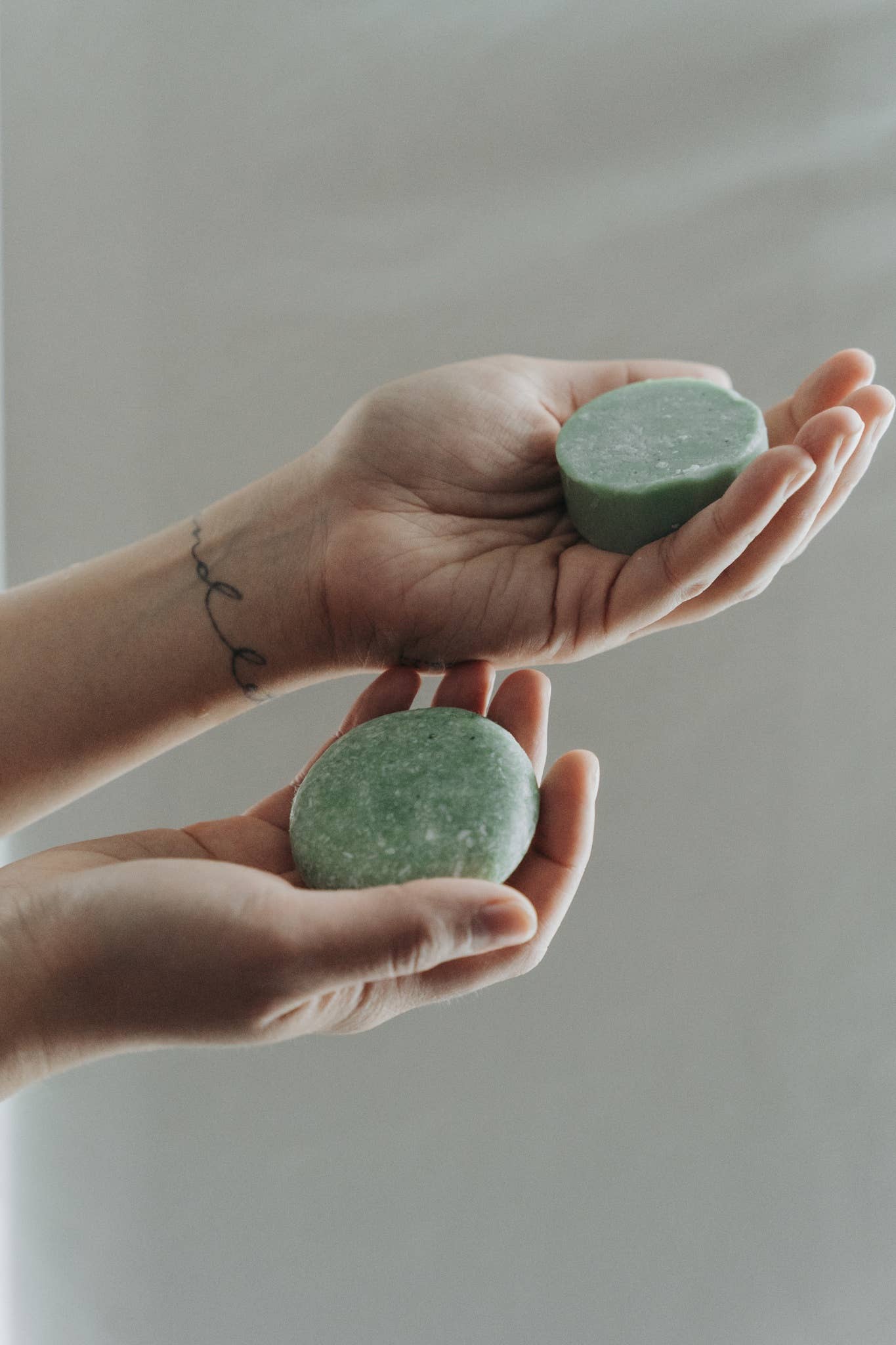 A person holds a sustainable peppermint and eucalyptus solid conditioner bar in one hand, and a matching shampoo bar in the other