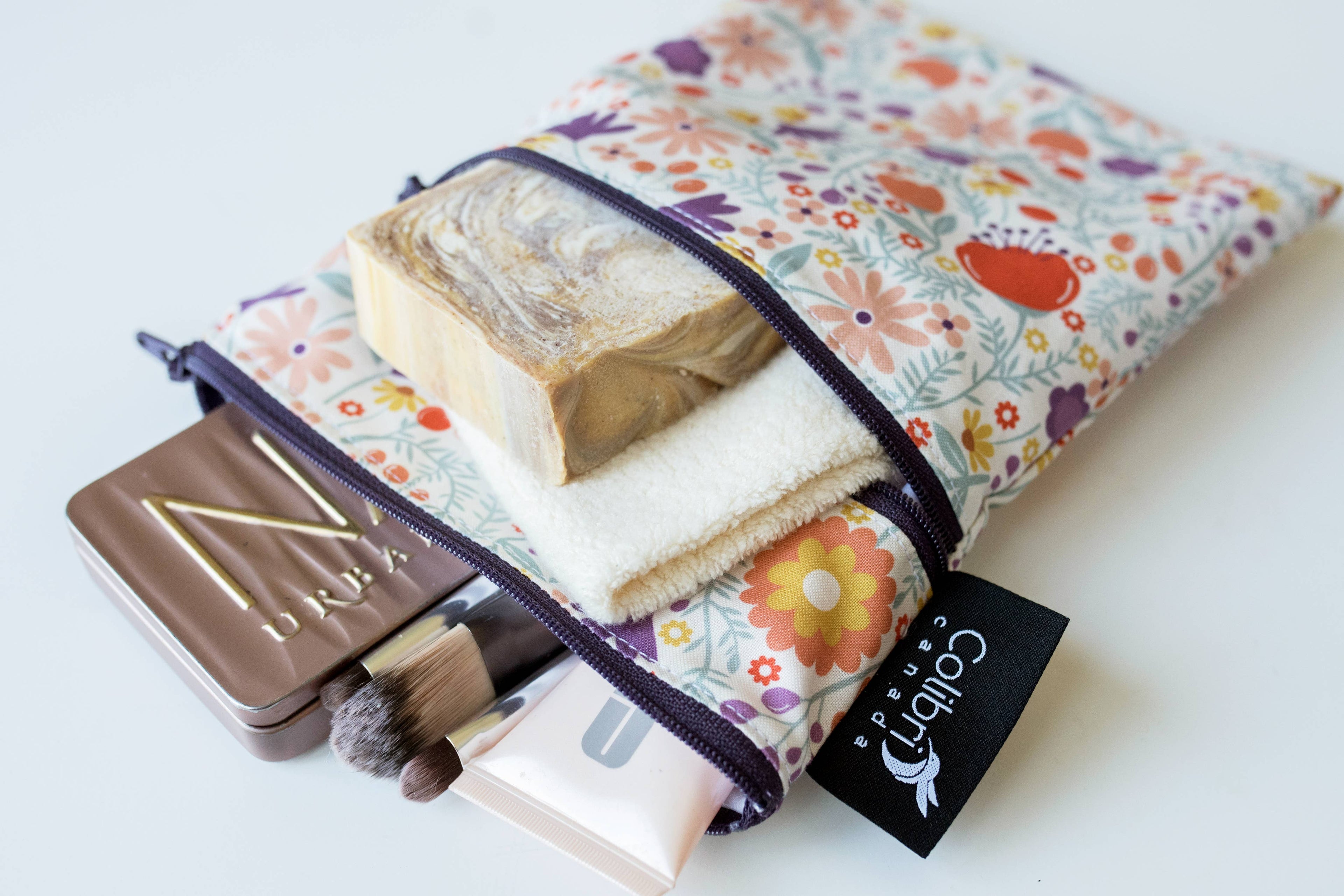 A small reusable multi-purpose bag with flower-motif fabric holding a variety of makeup and toiletries