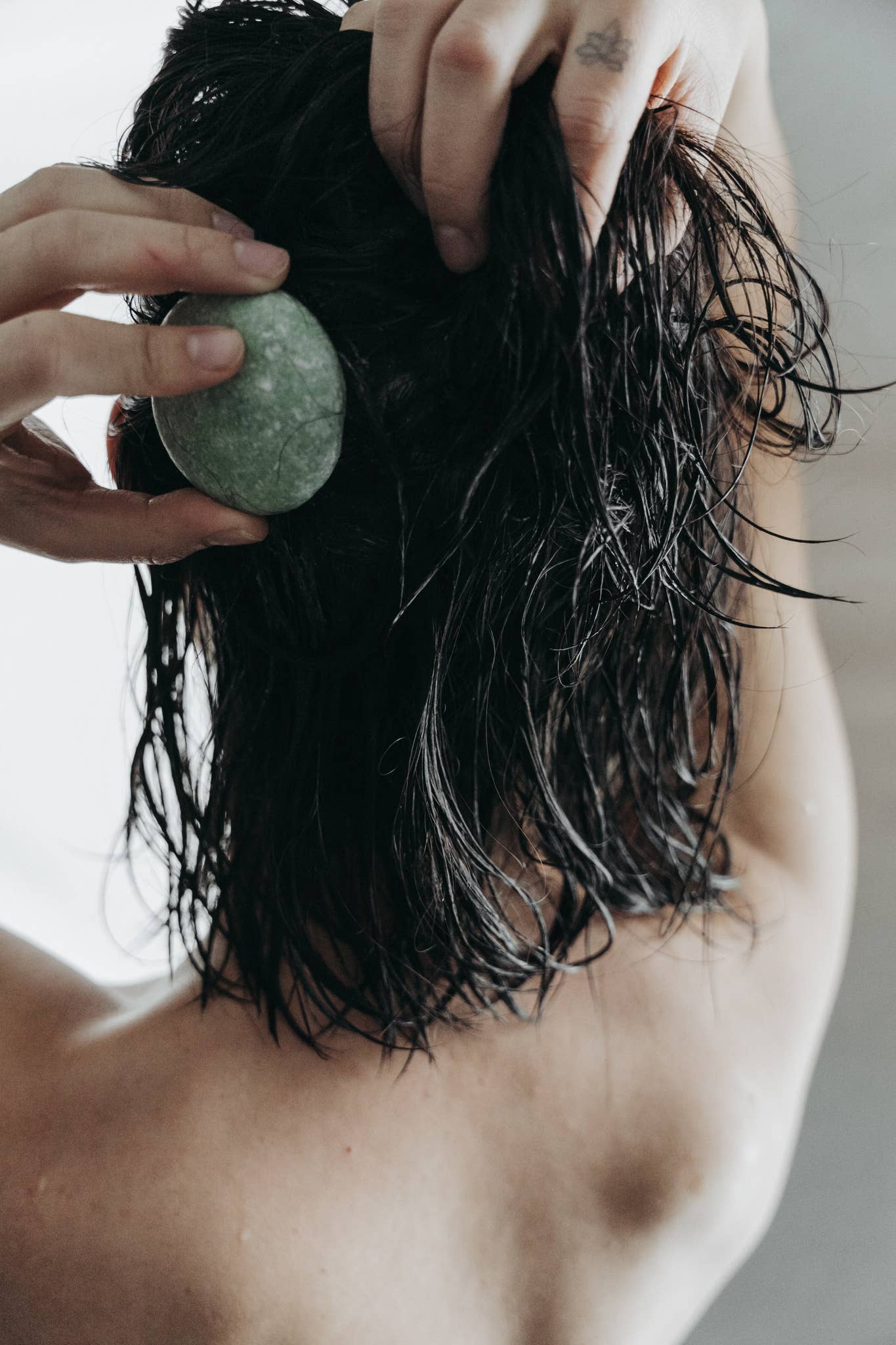 A person applying the sustainable solid shampoo bar to their wet hair