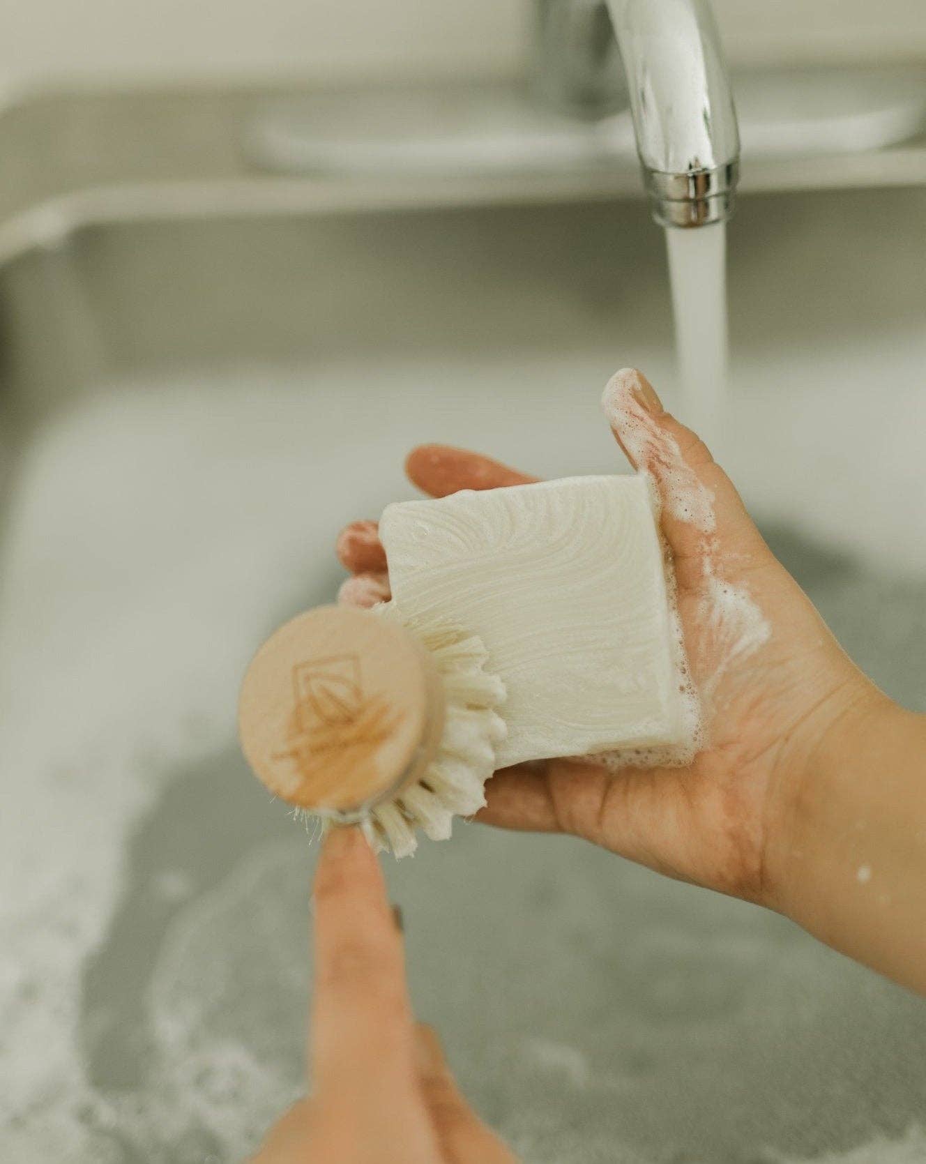 A person lathers a natural dish brush using a sustainable solid dish soap bar