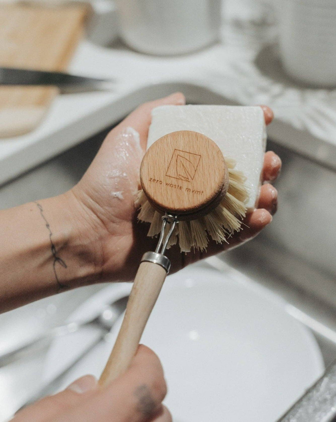 A person lathers a natural dish brush using a sustainable solid dish soap bar