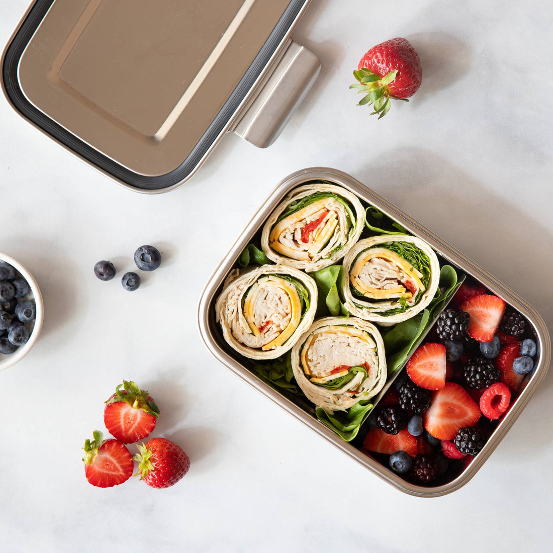 A large size stainless steel bento box holds 4 wraps and a variety of berries with a separator between them