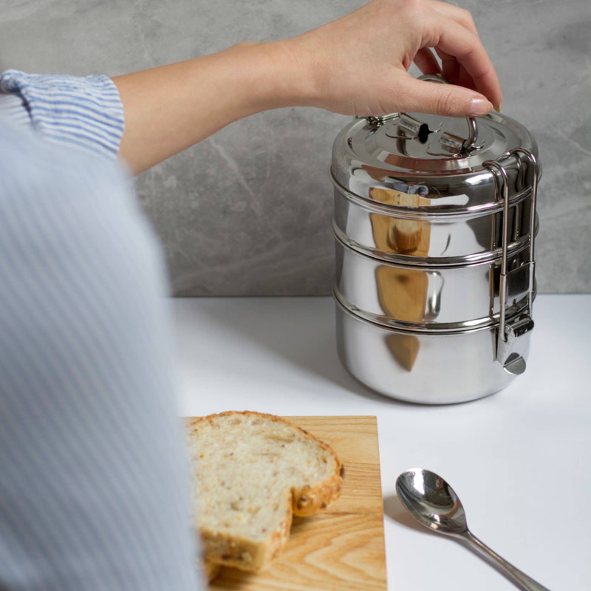 A person using a three-tiered tiffin container set