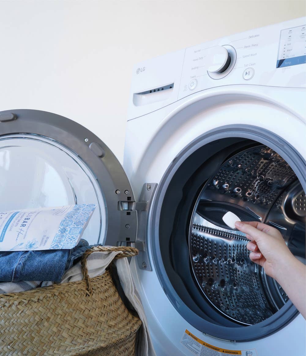 A person puts a TANIT laundry detergent tab into a front-load washing machine